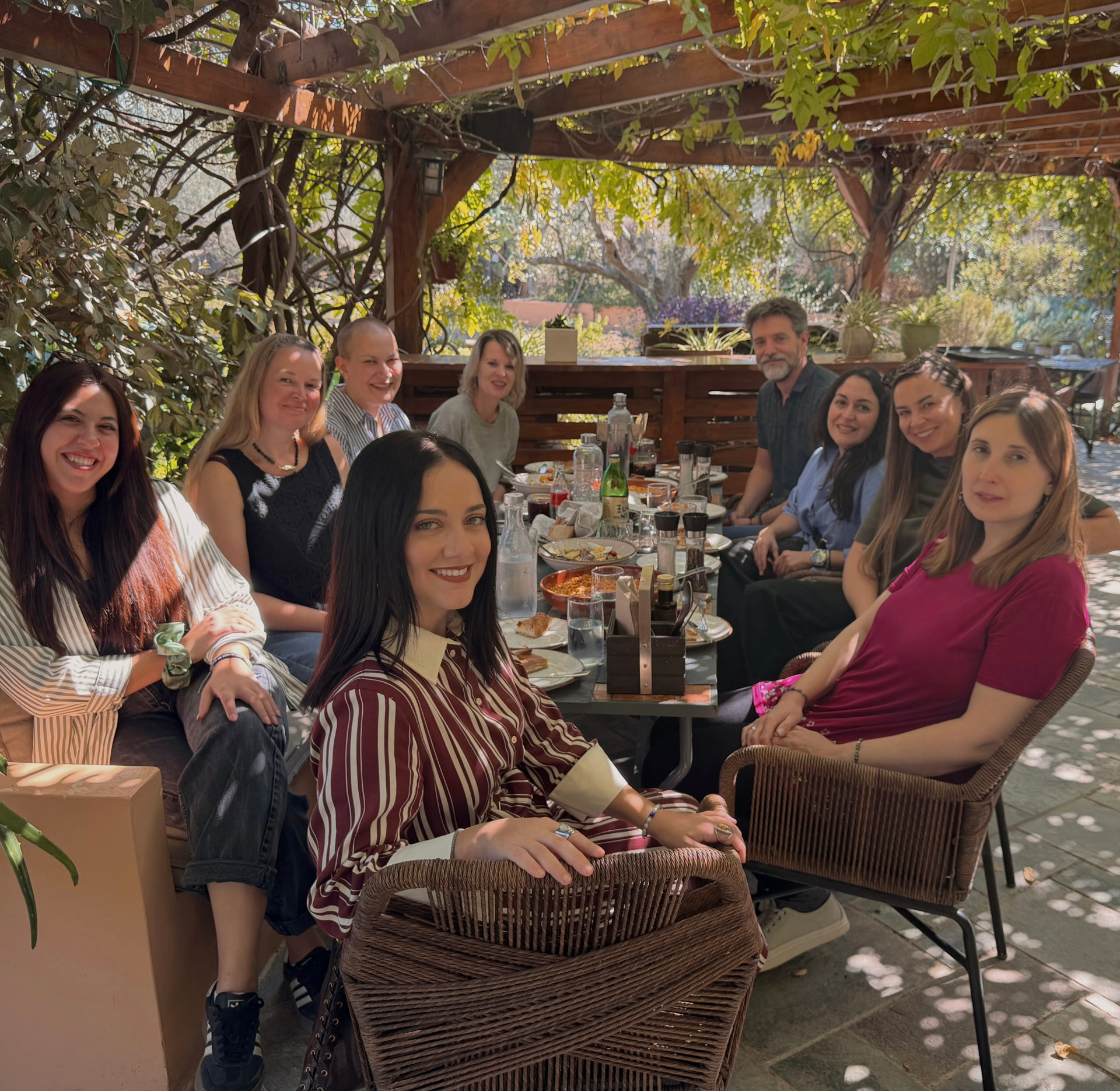 Nine MindWavers posing together around a lunch table under a vine-covered pergola