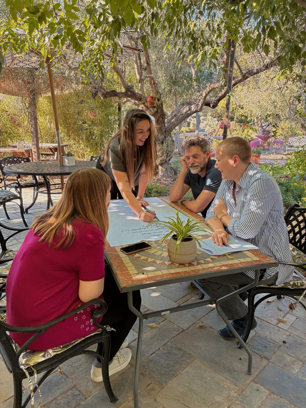 Four MindWavers working together on a sheet of notes around a table in a garden