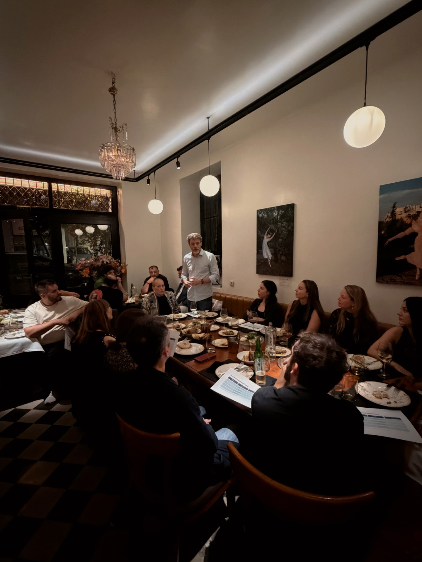A MindWaver standing to address colleagues seated along a long banquet table at an evening dinner