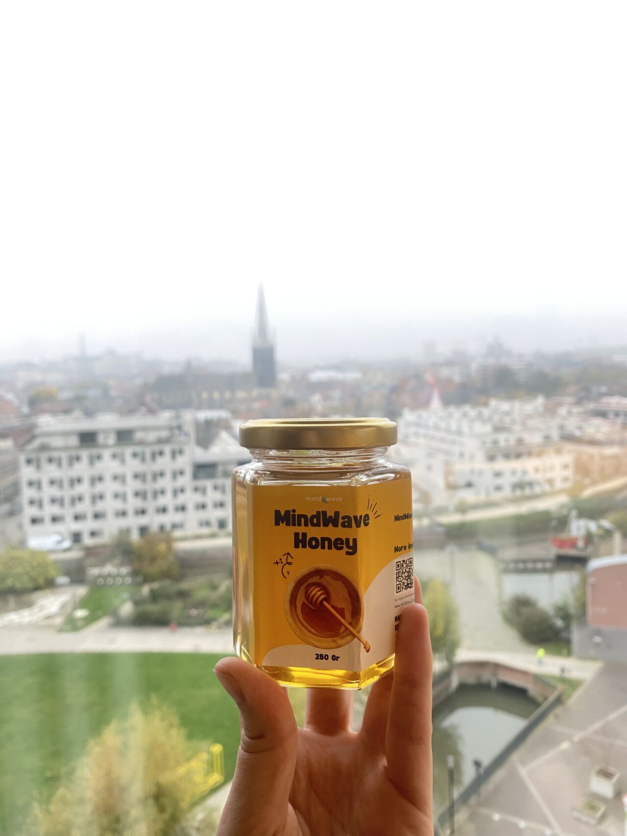 A jar of MindWave Honey held up in front of the Leuven skyline